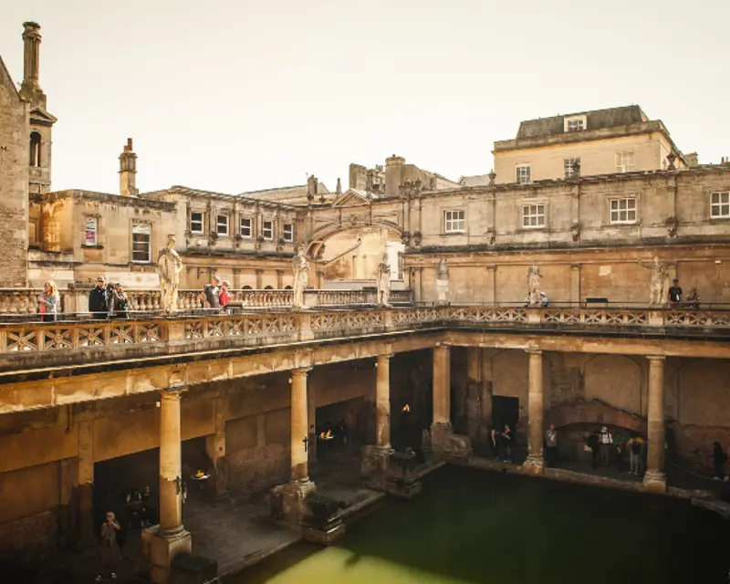 Historic Roman baths in Bath, UK, featuring classical architecture and visitors exploring the serene water.