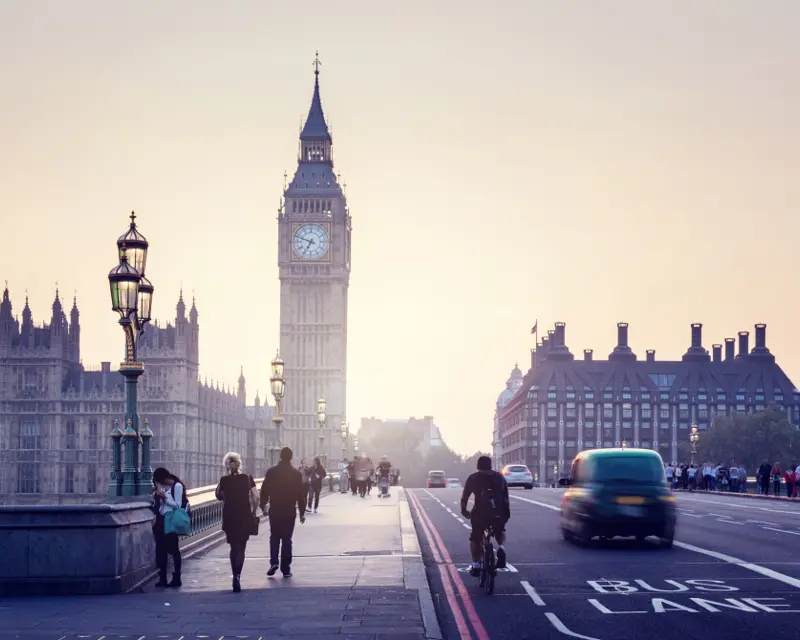 Iconic view of Big Ben at dusk with pedestrians and traffic on Westminster Bridge, showcasing London's vibrant atmosphere.