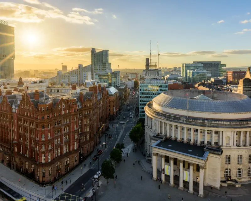 Sunset over a cityscape featuring a mix of historic and modern architecture, with bustling streets below.