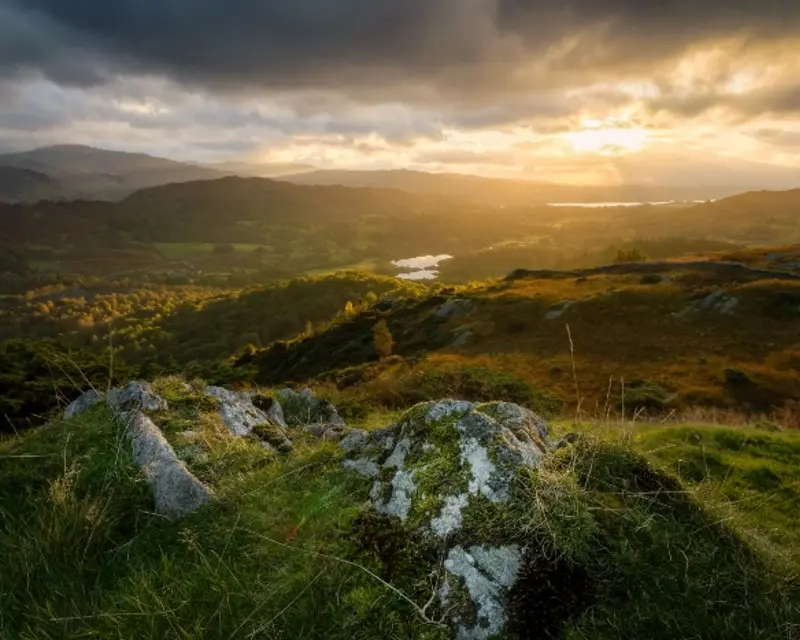 Scenic landscape at sunset with rolling hills, rivers, and a dramatic sky, showcasing the natural beauty of the UK for tours.