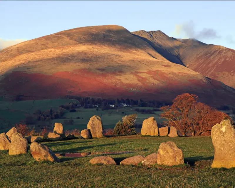 Ancient stone circle against a backdrop of rolling hills under a clear sky, showcasing the beauty of the UK countryside.