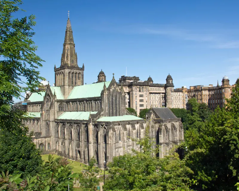 Glasgow Cathedral with its intricate architecture and green surroundings, framed by a clear blue sky and historic buildings.