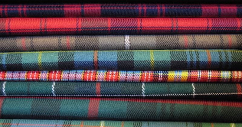 different coloured clan tartans folded and stacked in a pile