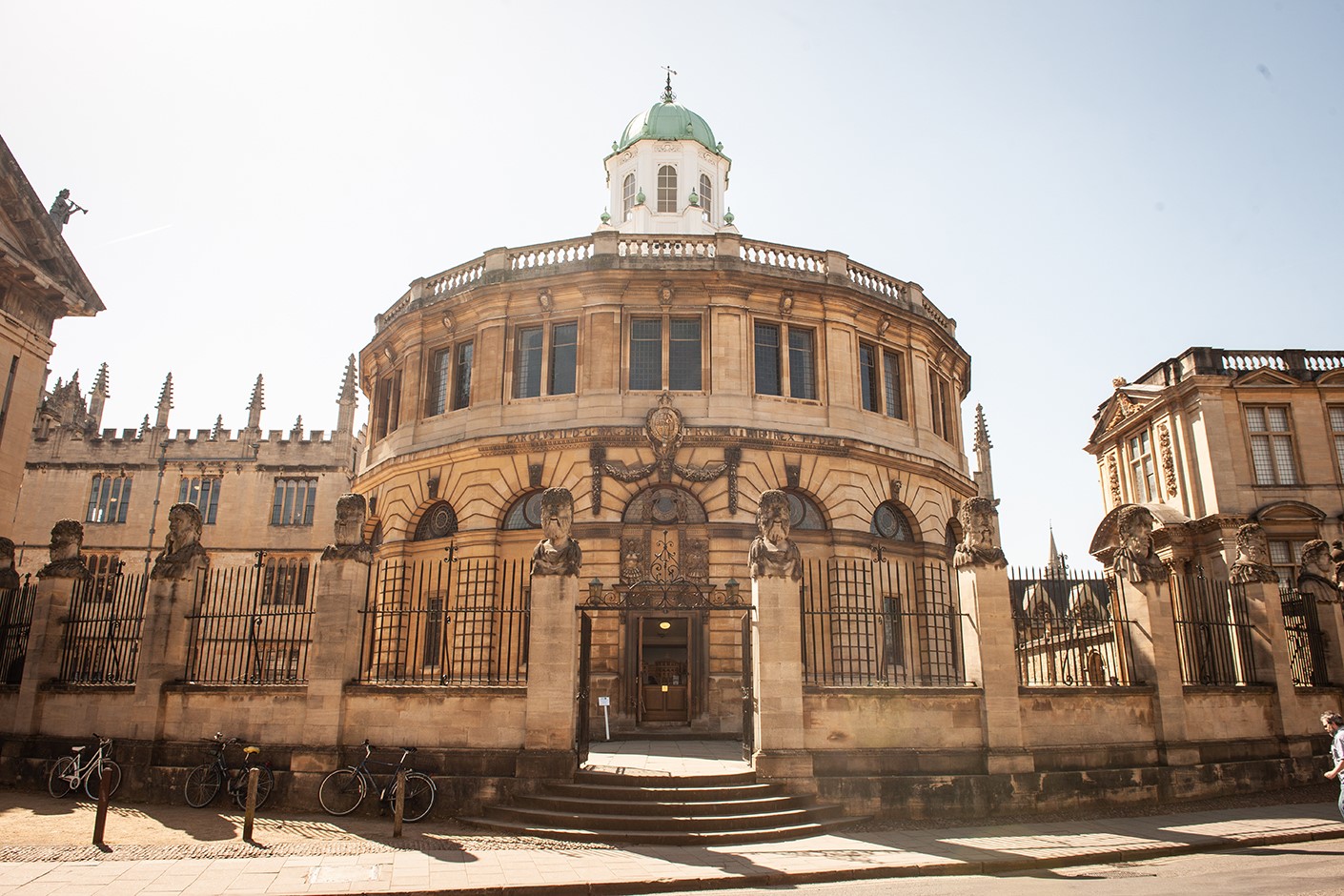 A round stone building in Oxford with a green domed roof and a walled fence guarding the front 