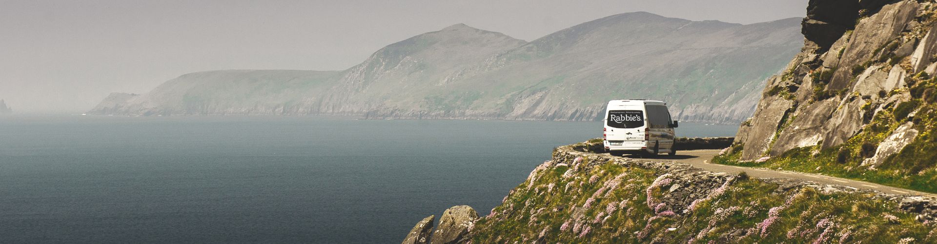 Rabbie's tour bus driving along a narrow coastal road.