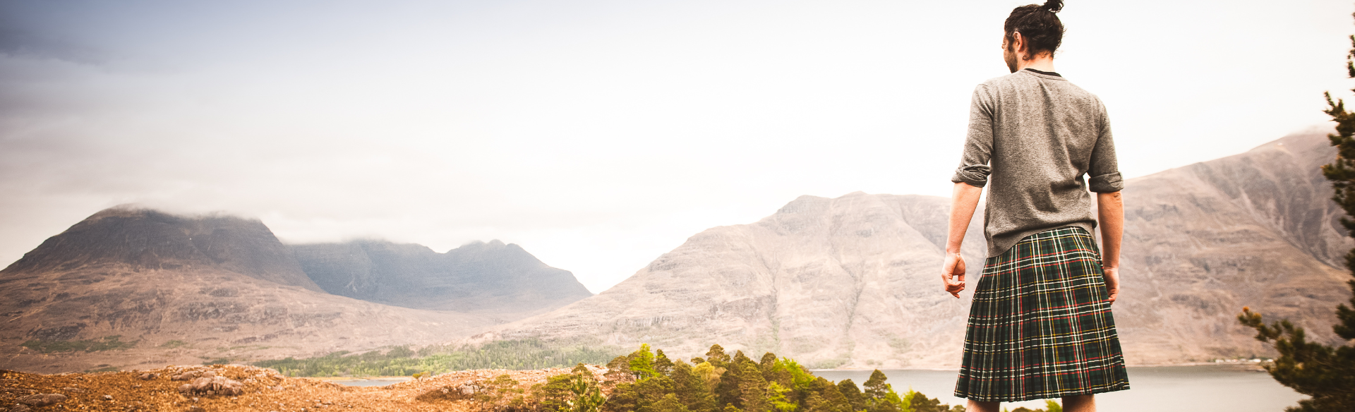 a man in a kilt standing on a rock looking at a view