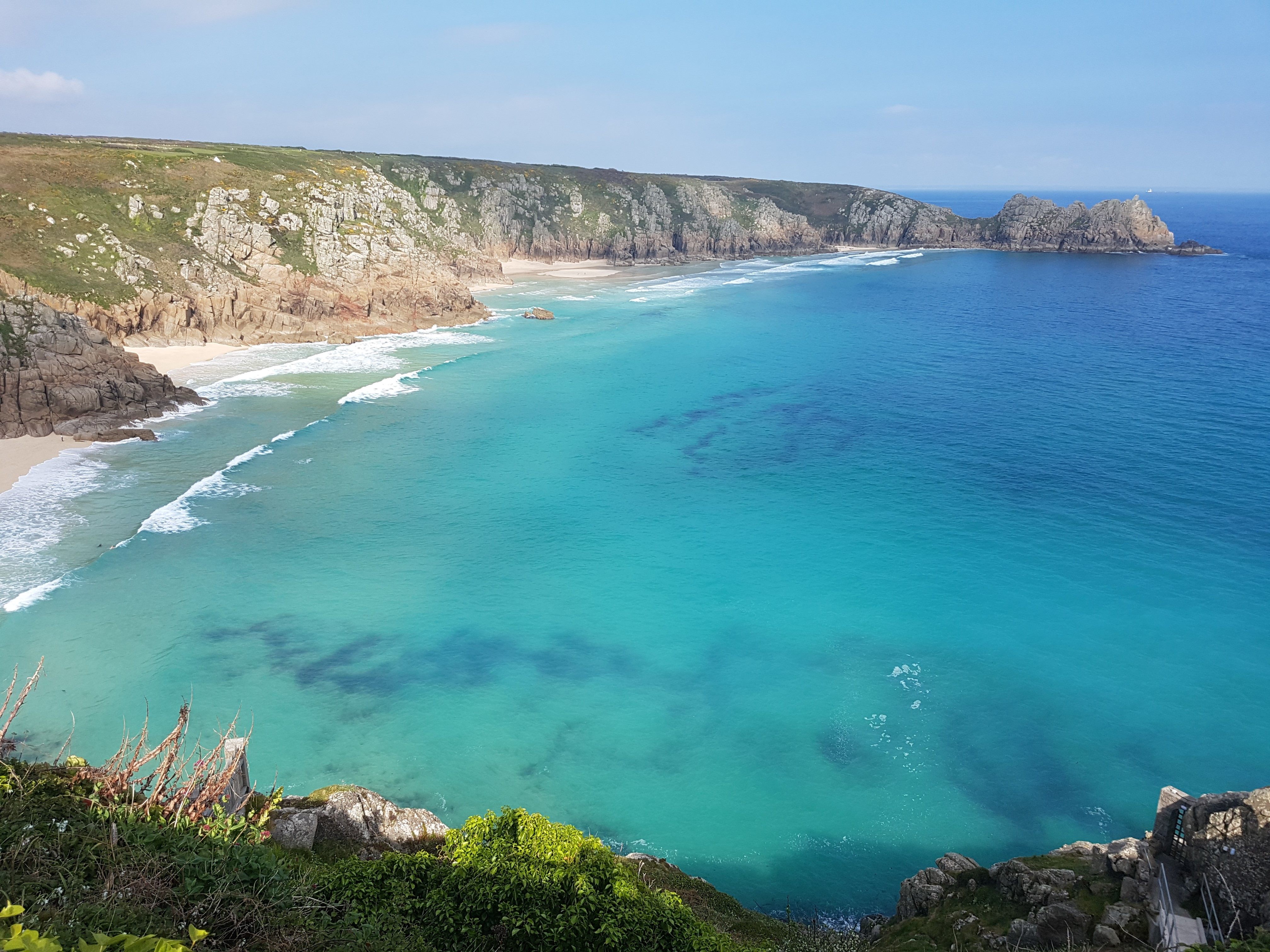 Porthcurno beach landscape with rocky mountains to the left and clear turquoise waters to the right