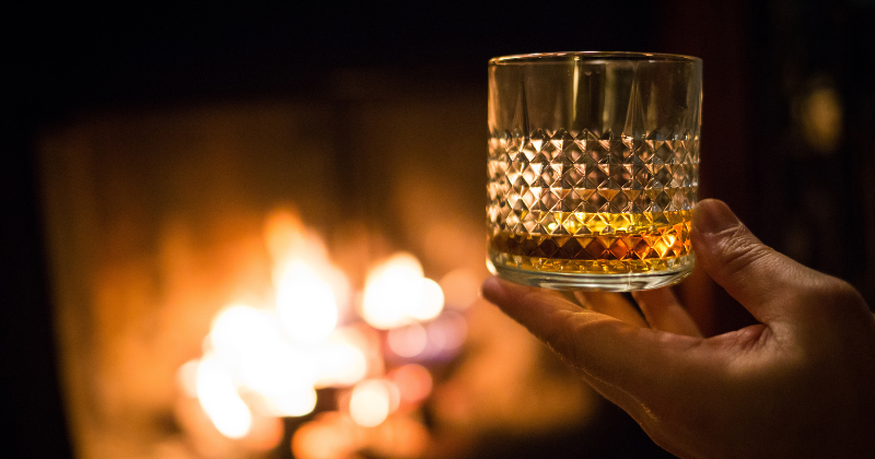 Whisky glass being held by a hand before a fireplace