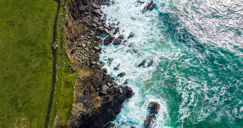 A birds eye view of a road and cliff and the ocean