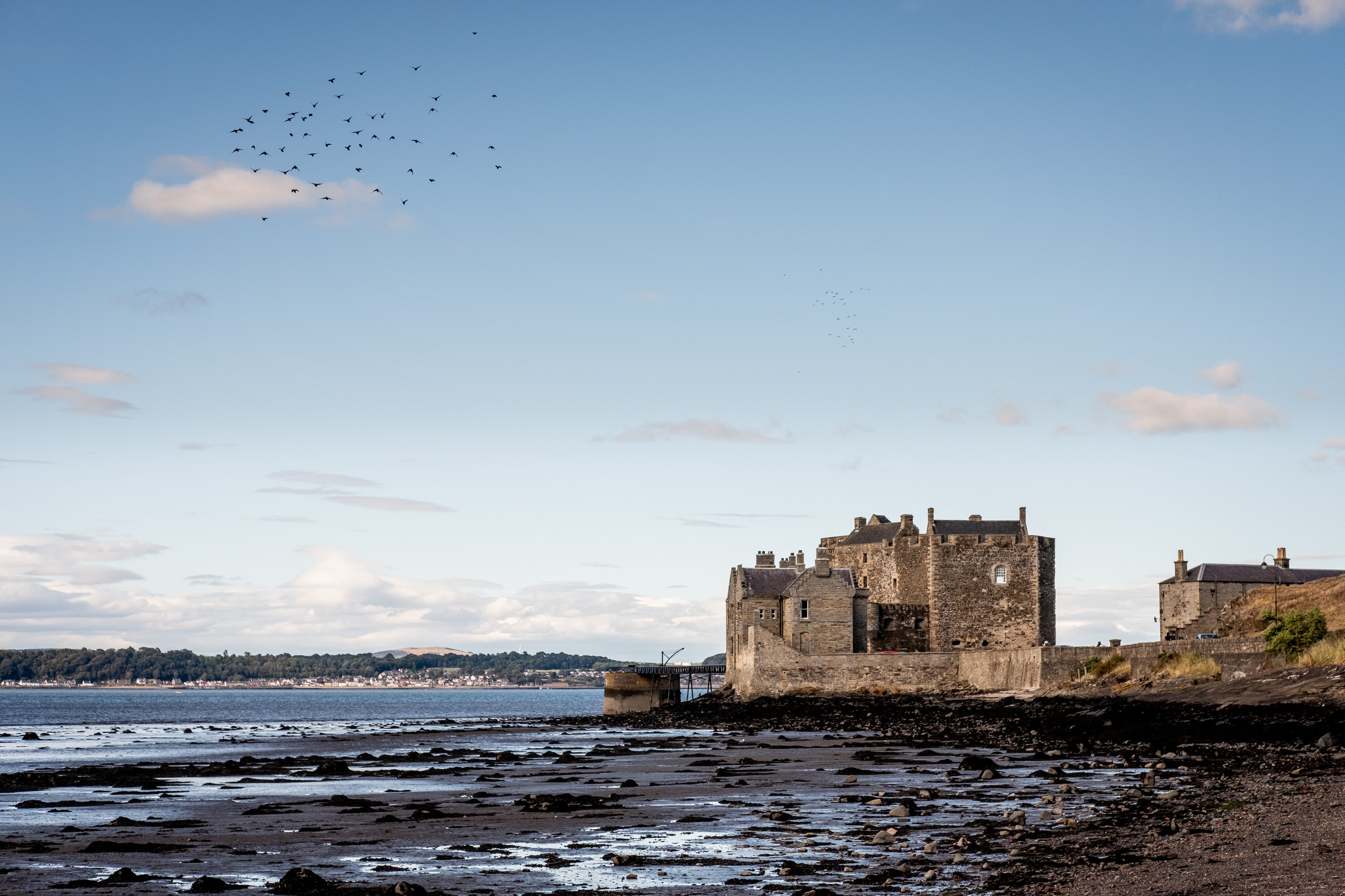 Blackness Castle surrounded by dark blue waters, pale blue skies overhead which feature a flock of black birds