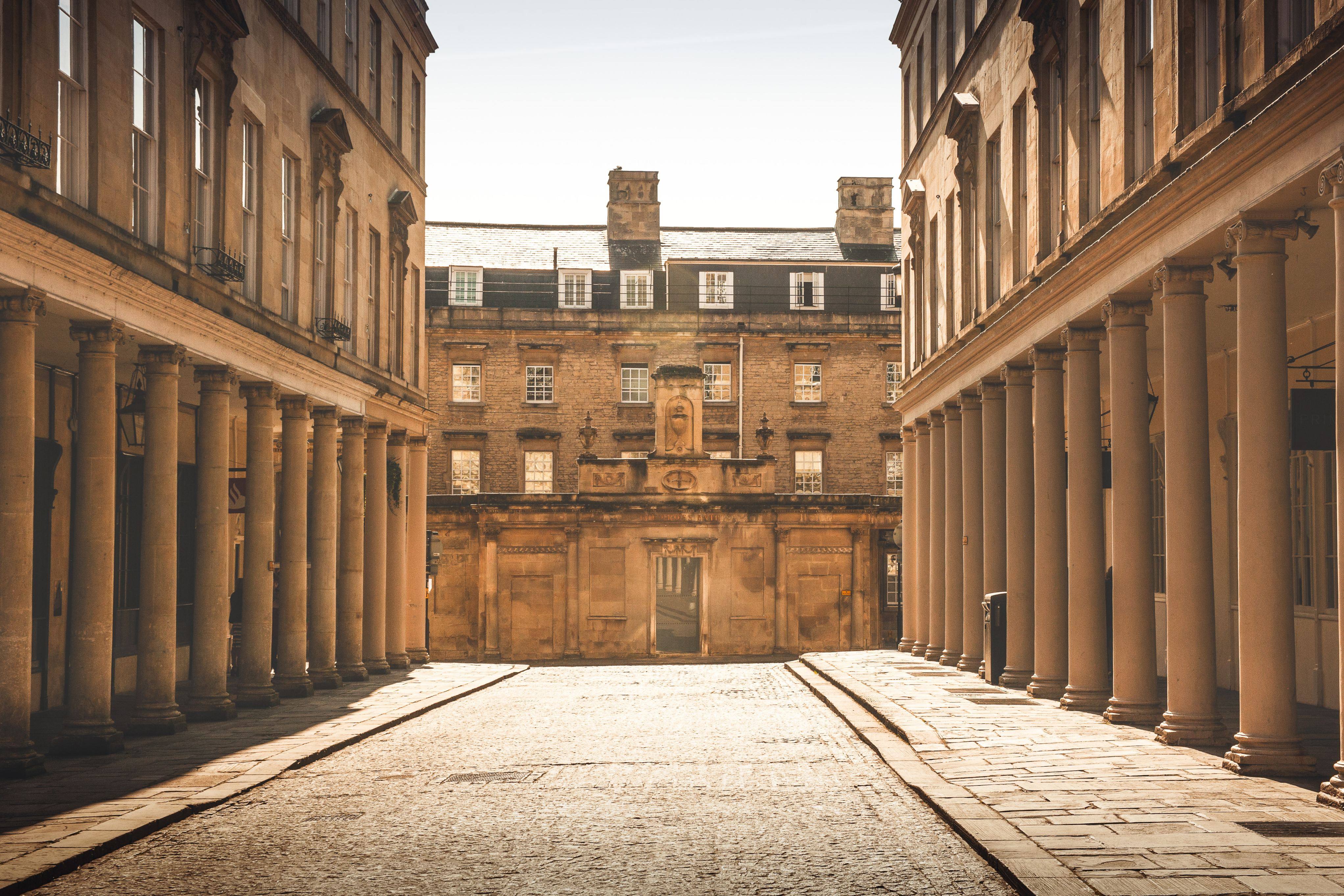 Bath’s cobbled street, with a building in front of you and a building to the left and right in a light sand colour