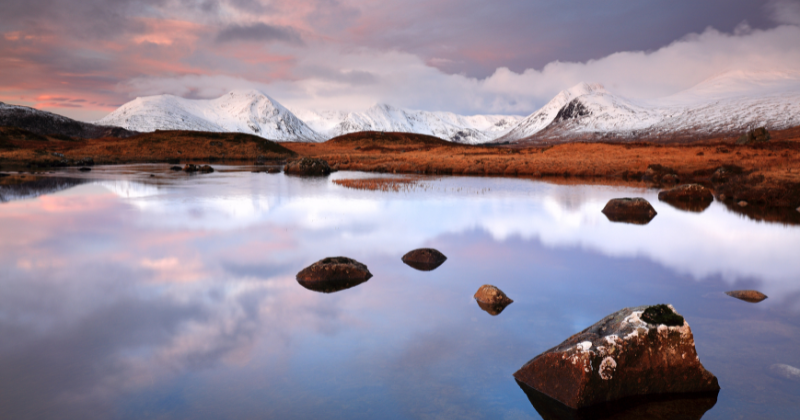 A loch overlooked by snow-covered mountains in Glencoe in Scotland