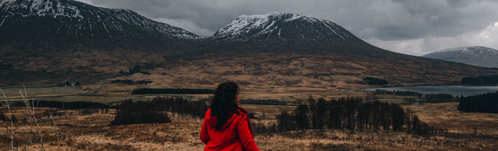 Girl standing in a red coat looking over a dramatic landscape