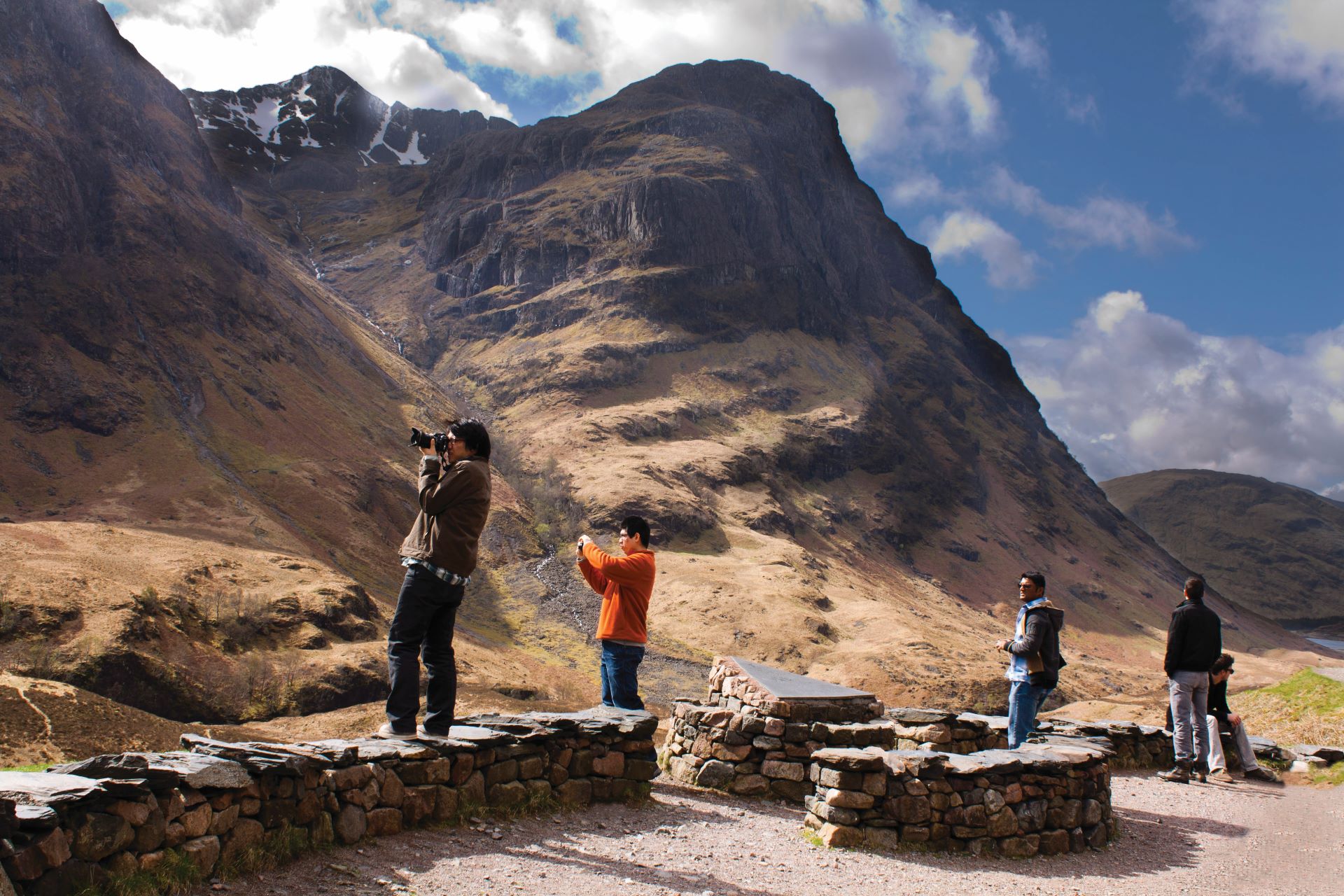 A group of people standing in Glencoe taking photographs of the scenery.